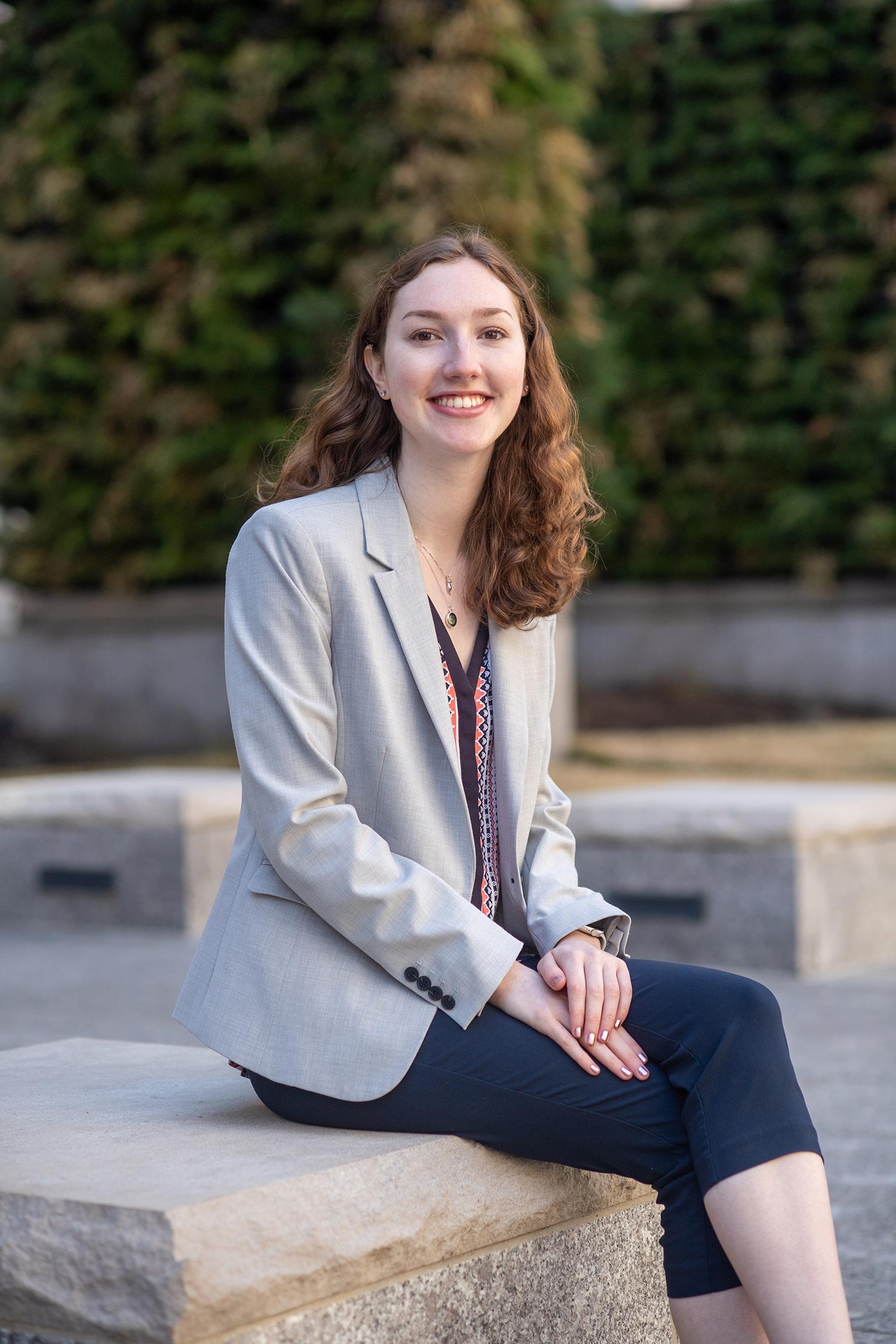 Photo of Nicole Somerstein (Questrom’21) in a gray blazer, smiling, with her strawberry blonde hair down, sitting on a granite bench.