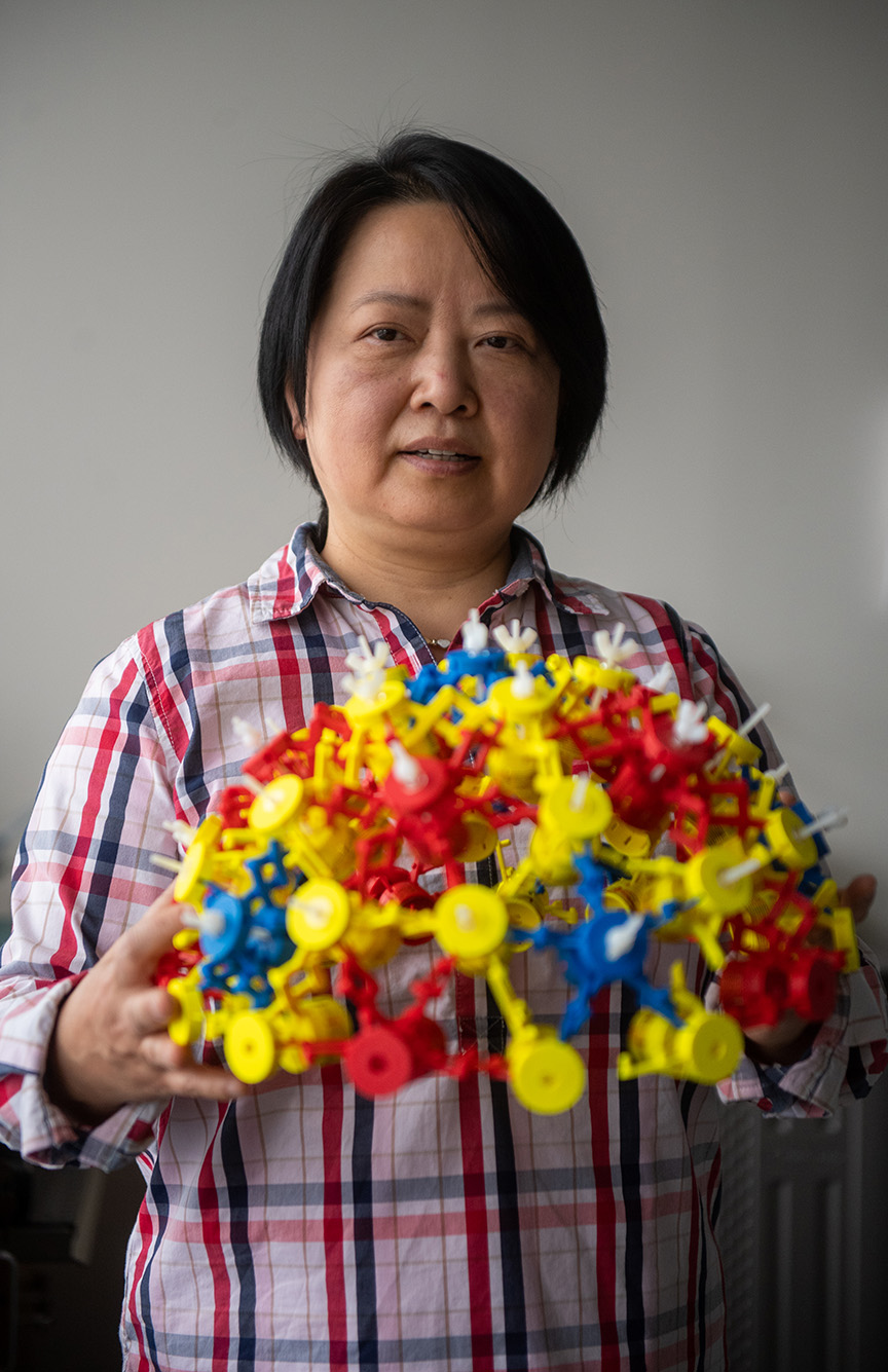 Boston University Professor of Engineering, Xin Zhang, poses for a portrait in her lab. She holds a magnetic Metamaterial device. The hat is made of materials in red, yellow, and blue.