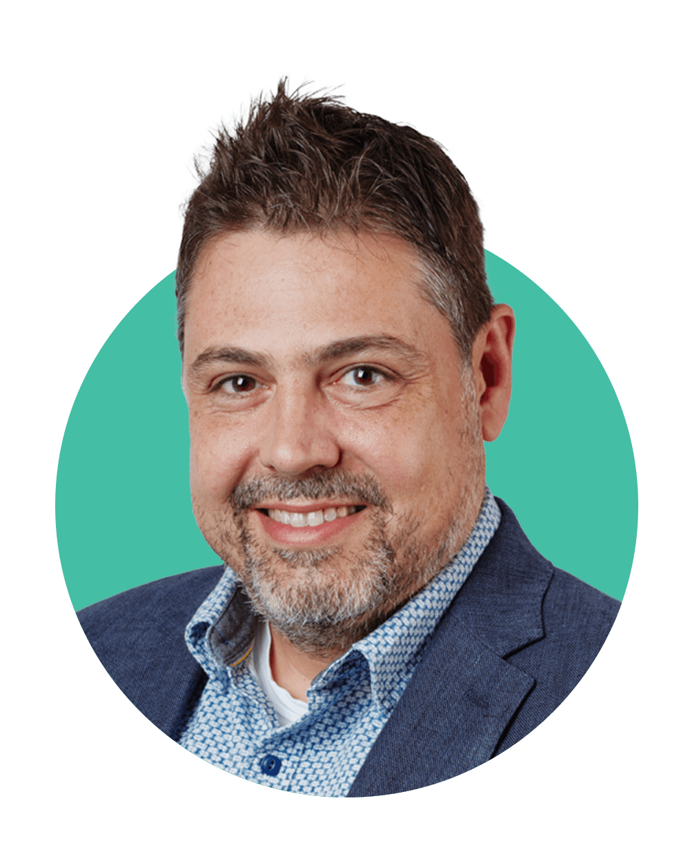 Photo of Basilis Zikopulous, a middle-aged man with short, spiky brown hair. He wears a blazer and blue shirt and smiles. His head is framed with a decorative teal circle.