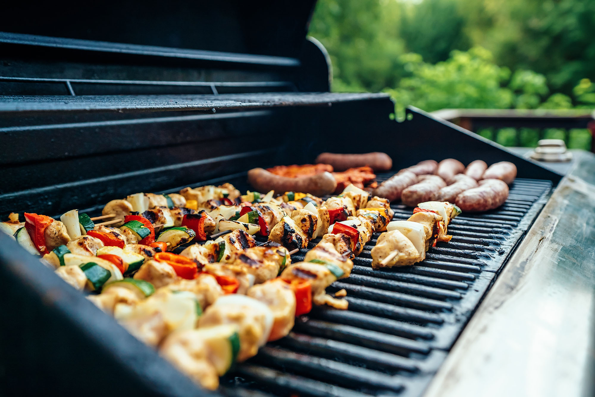 Photo of chicken kebabs and sausages on a propane grill.