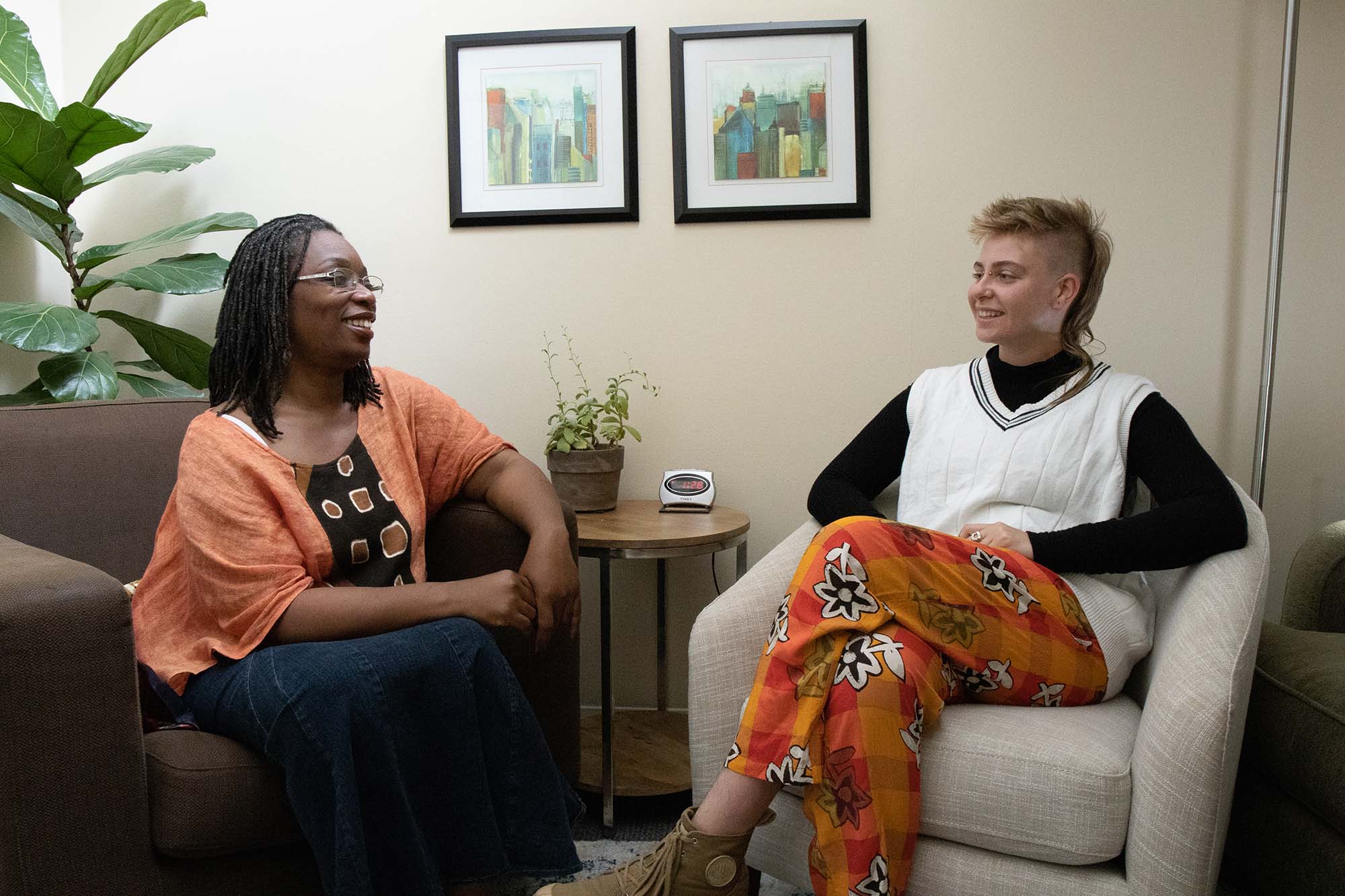 Photo of Somerville (left) and Sage Institute therapist Z Shmueli (right) “in session” at Sage offices. They both sit on comfy armchairs and face each other in the office as they pose for the camera.