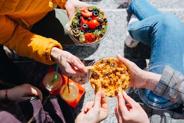 a group of friends sharing a bowl of guacamole outside. Only their hands and the guac are visible.