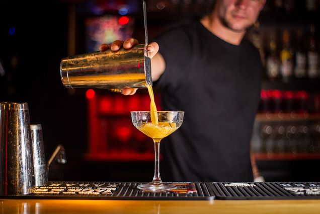 A bartender pours a cocktail out of a shaker and into a high glass