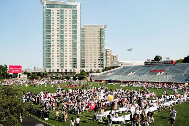 Wide photo of Nickerson field during the annual SPLASH event. Students walk across the field to look at the tables set up by BU student clubs. STUVII is seen in the background; the sky is blue and clear.