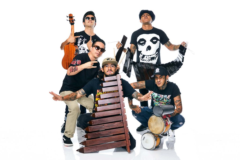 Photo of Mexican group Son Rompe Pera posting with their musical instruments. The group is comprised of fiven youngish men of color, all of them with arm tattoos. Two hold instruments that look like xylophones , one holds a small guitar, another a set of handle held drums.