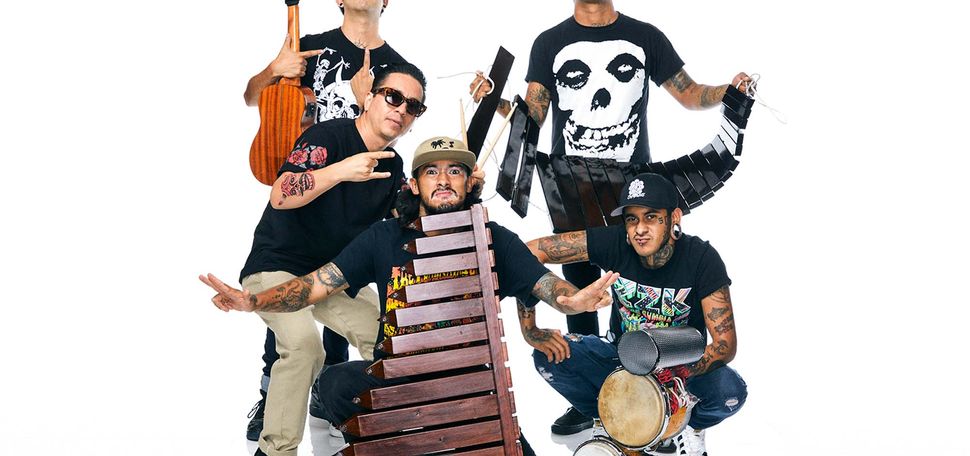 Photo of Mexican group Son Rompe Pera posting with their musical instruments. The group is comprised of fiven youngish men of color, all of them with arm tattoos. Two hold instruments that look like xylophones , one holds a small guitar, another a set of handle held drums.