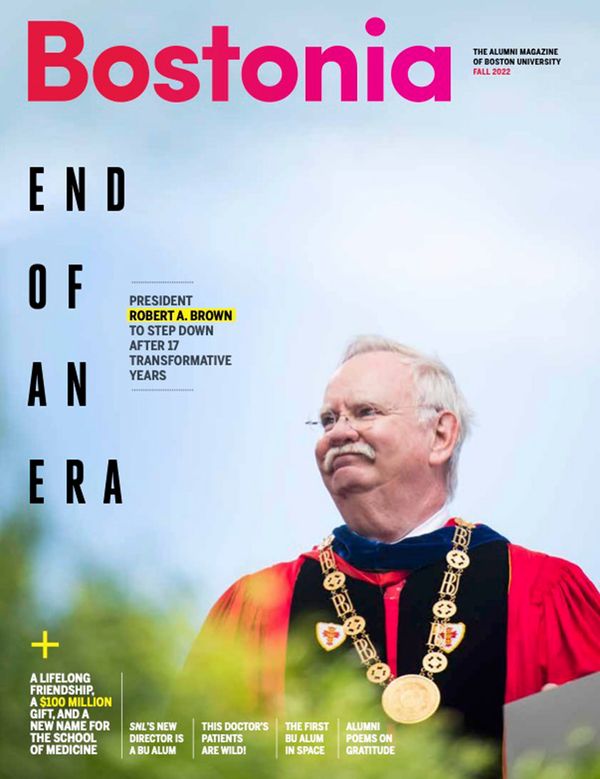 Cover of the Fall2023 edition of Bostonia. The cover features a photo of BU President Robert Brown looking to the left and smiling. He wears frameless glasses, a red ceremonial graduation robes with black and blue velvet stoles adorned on him. He also wears a golden, ceremonial BU necklace. Background shows a light blue, clear day. The cover reads “Bostonia. End of an Era. President Robert A. Brown to step down after 17 transformative years”. Along the bottom, the cover reads in smaller text “A lifelong friendship, a $100 million gift, and a new name for the school of medicine. SNL's new director is a BU alum. This doctor's patients are wild! The first BU alum in space. Alumni Poems on Gratitude.”