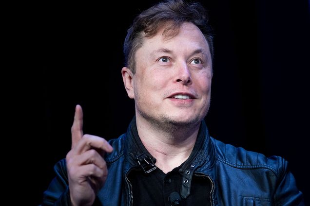 Photo: Elon Musk, a white man with thinning brown hair, looks and points up as he's shot mid-talk in front of a black background.