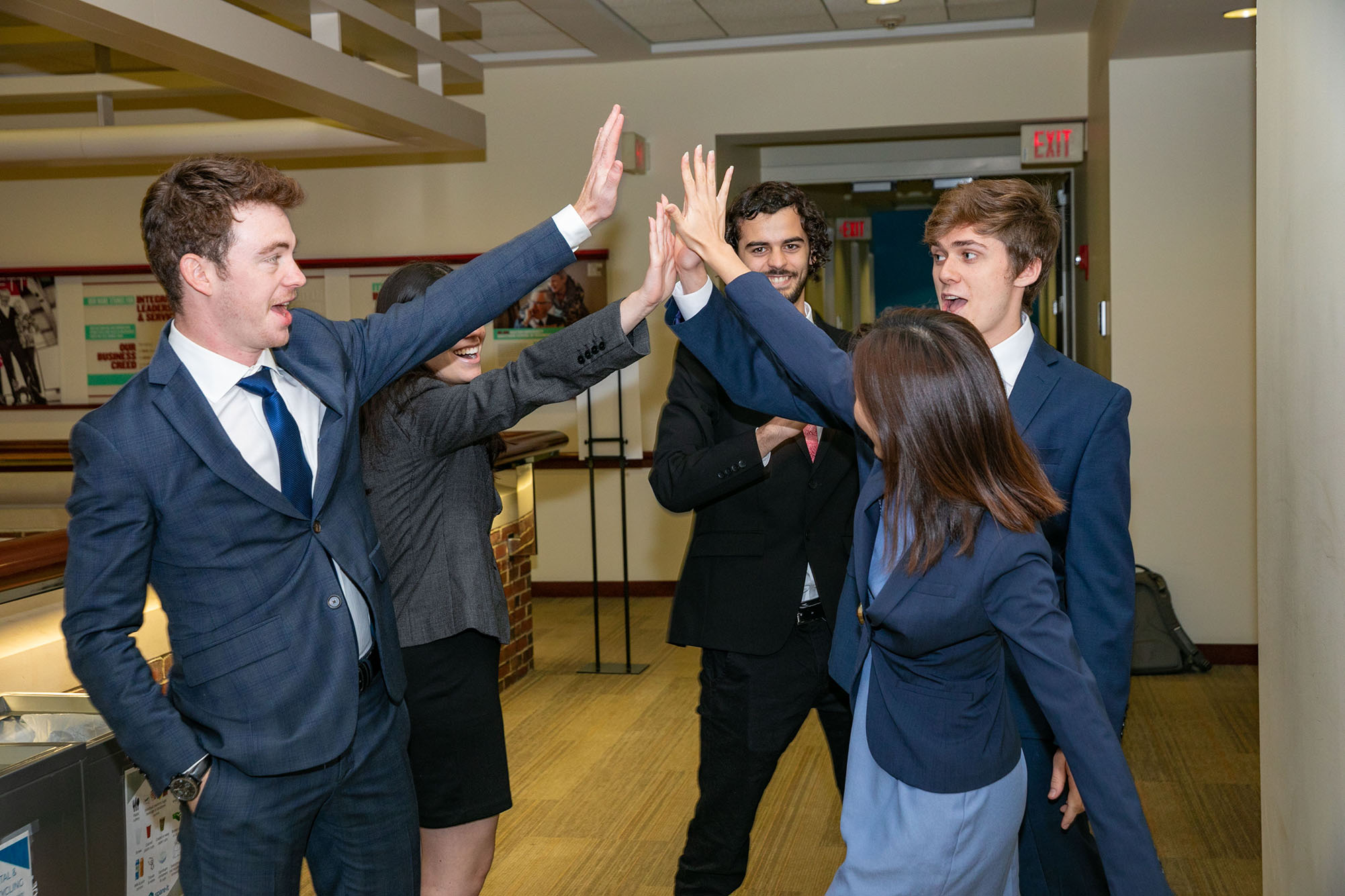 Photo of a group of five students, all wearing suits, high-fiving each other.