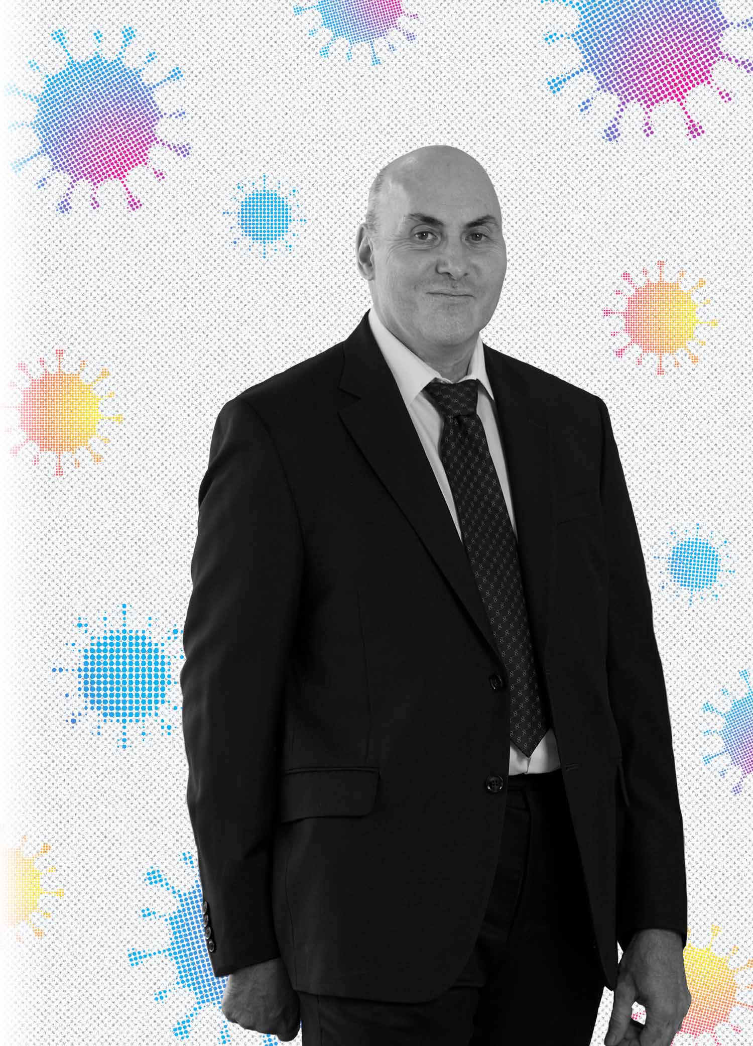 Black and white portrait of Drew Weissman (MED’87, GRS’87), smiling, in a black suit. A background with blue, purple, yellow and orange gradient coronavirus molecules are seen behind him.