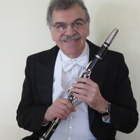 Photo: Edward Avedisian, an older Armenian man in a white collared shirt and black suit jacket, smiles as he holds a clarinet in his hands.