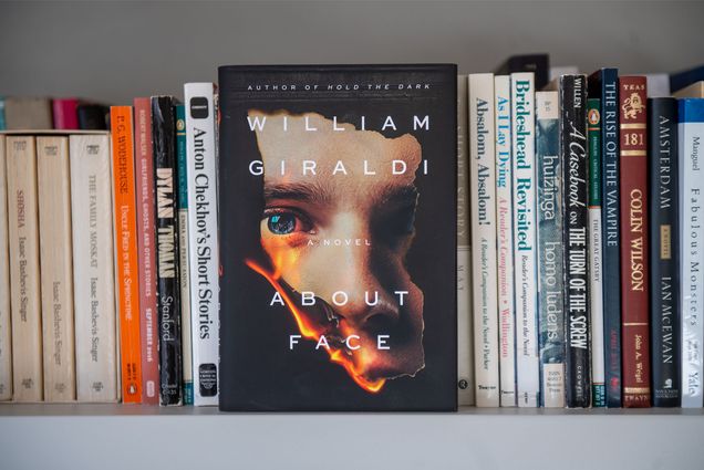 The cover of "About Face" by William Giraldi. A man's face can be seen through what appears to be a burning hole in the book