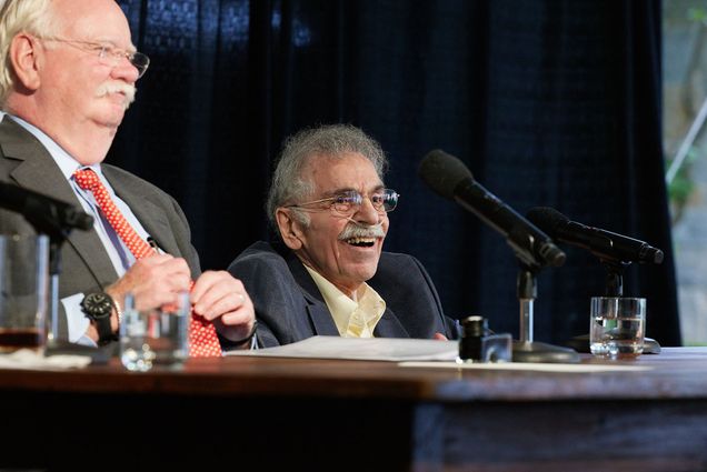Photo of President Brown and Edward Avedisian seated at a large, dark brown table one stage, smiling and looking off to the right at the crowd.