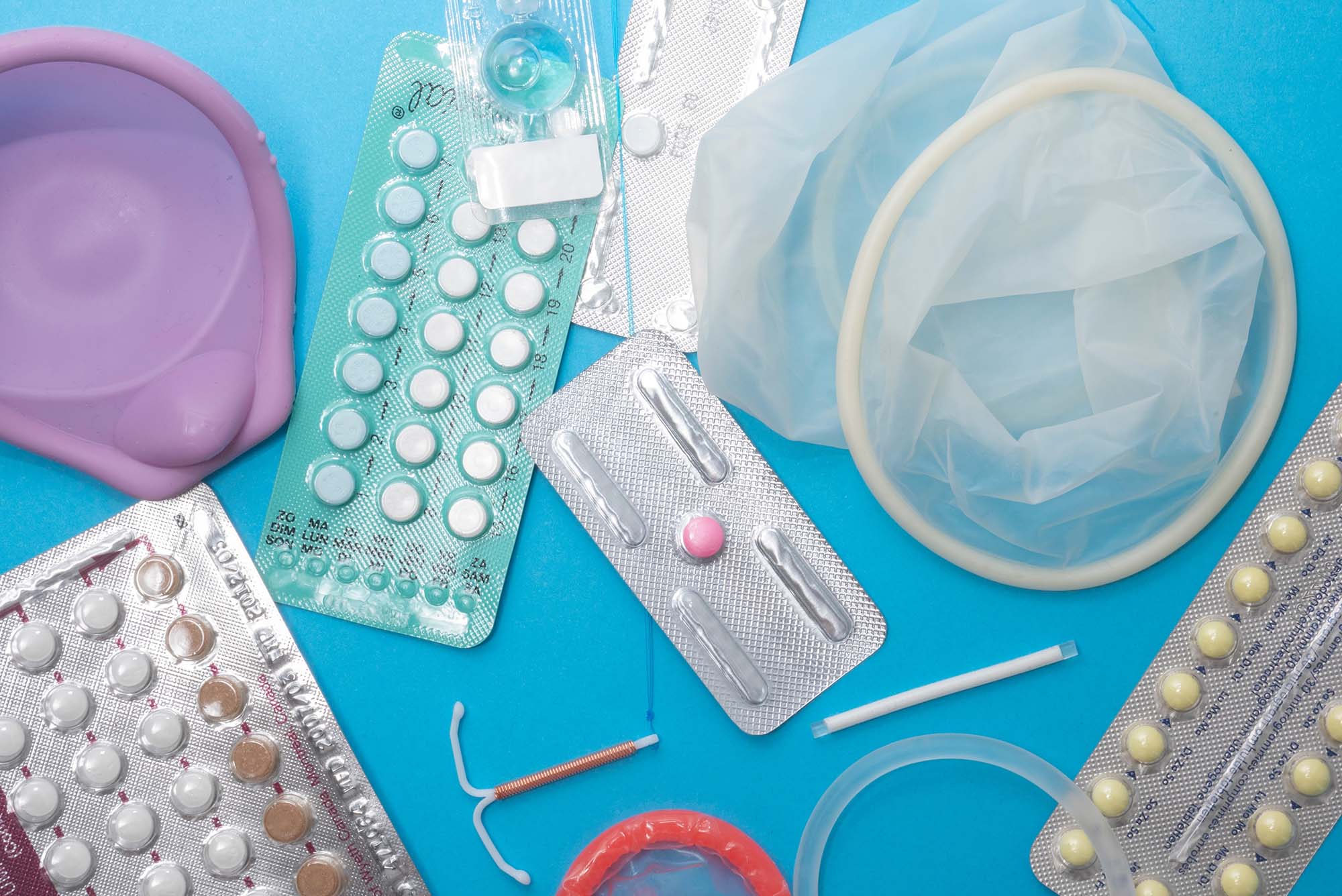Photo: Overhead shot of a selection of reproductive health supplies including:pills, diaphragm, condoms, vaginal ring, IUD, implant, dmpa, emergency contraception, and contraceptive pills. All the supplies lie on a lie background.