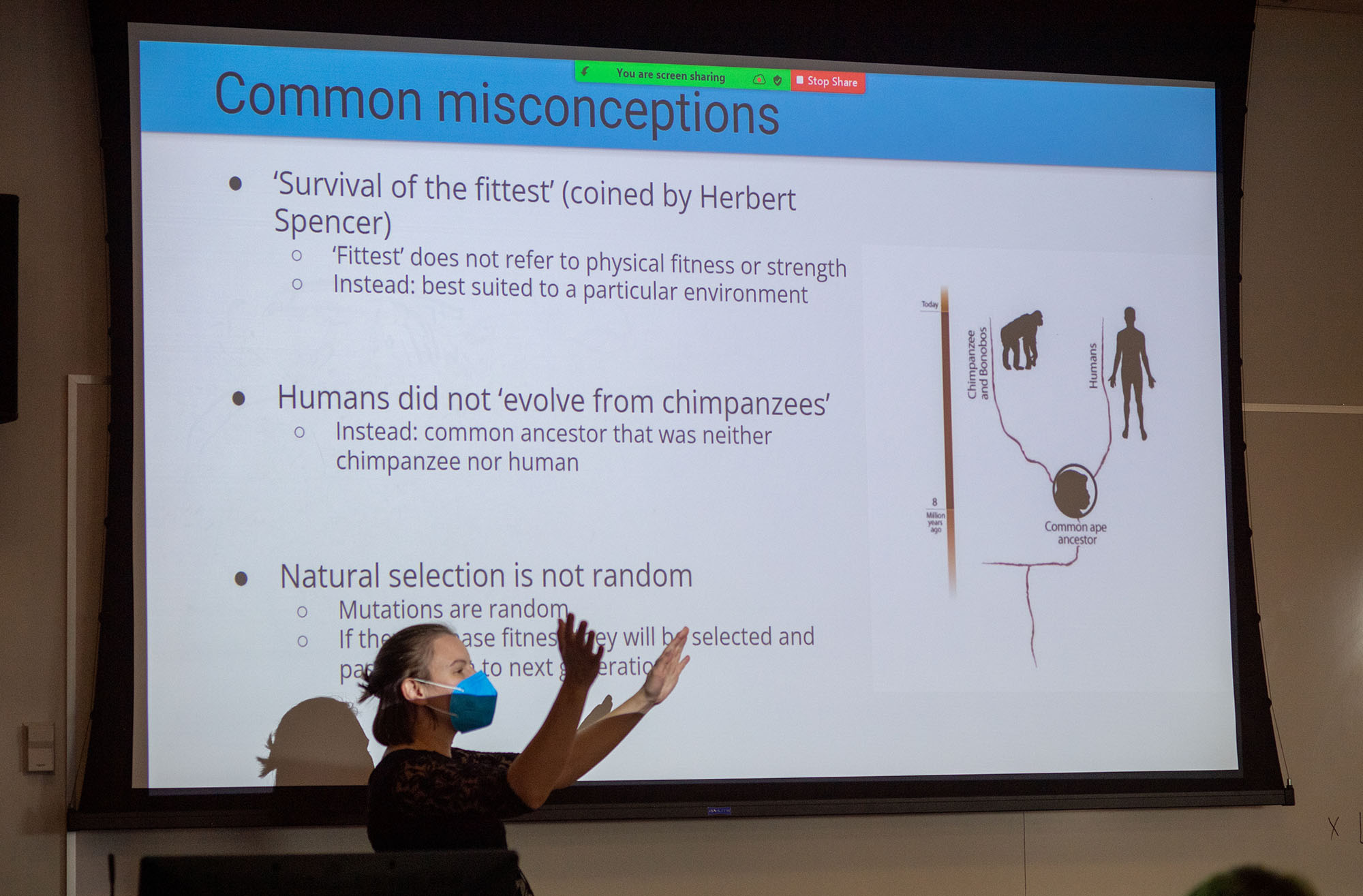 Photo: Melisa Osborne, a woman wearing a blue face mask and floral burgundy dress, leads a multi-disciplinary CAS class taking a look at the racism implicit in science and healthcare and trying to unpack it. She stands in front of a powerpoint projection showing common misconceptions in science.