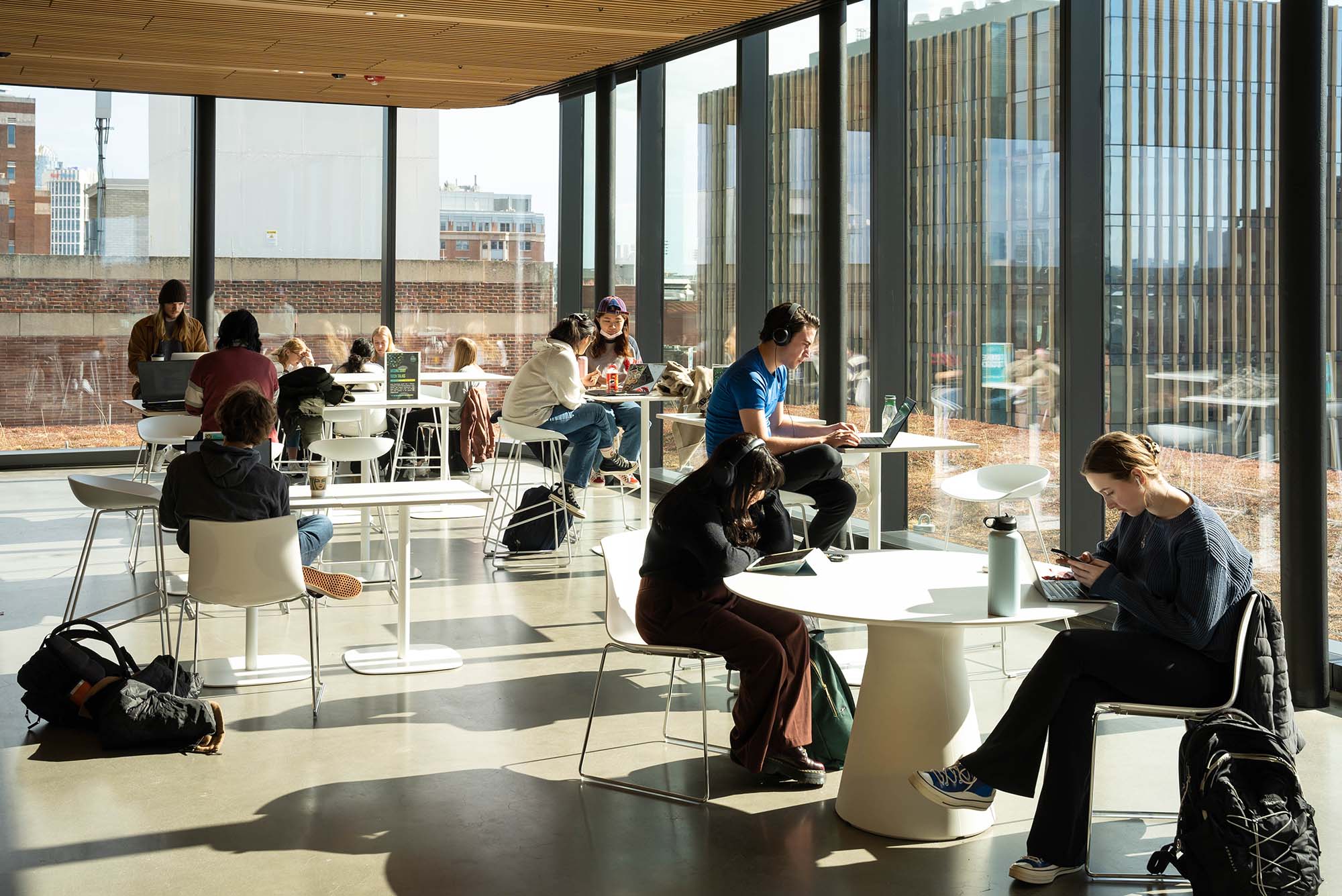 Photo: A sunny shot of the BU Faculty of Computing & Data Sciences Building as students sit and study at modern, round, white tables.