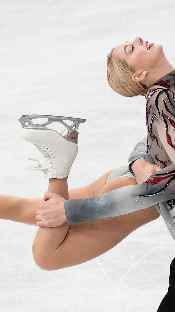 Photo: Alexa Knierim and Brandon Frazier of the U.S. perform during the pairs' short program in the World Figure Skating Championships in Saitama, Wednesday, March 22, 2023. A tall, white man wearing a grey and red themed figure skating outfit holds up a white woman with a similarly-styled figure skating outfit by her knee. They both have dramatic looks on their faces as they skate on the ice.