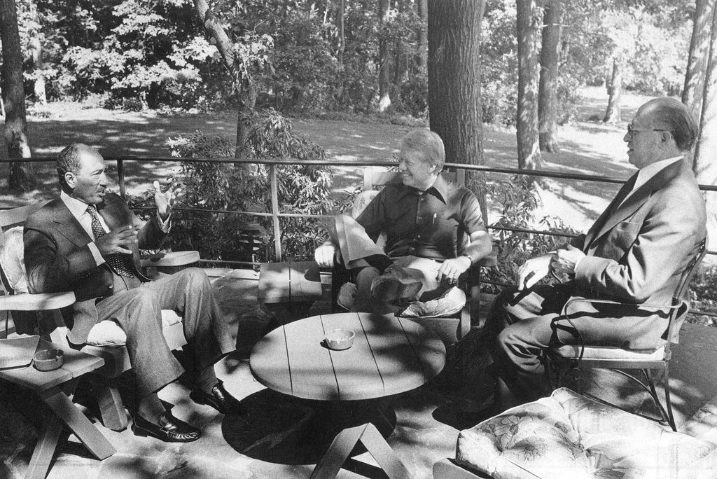 Photo: A black and white image of three men sitting at a table. From left, Egyptian President Anwar Sadat, U.S. President Jimmy Carter, and Israeli Prime Minister Menachem Begin, meeting for the first time at Camp David, Md., in September 1978, as they tried to hammer out a peace agreement between the two mideast countries that proved one of Carter’s greatest accomplishments. They are all smiles. They sit amongst a forest.