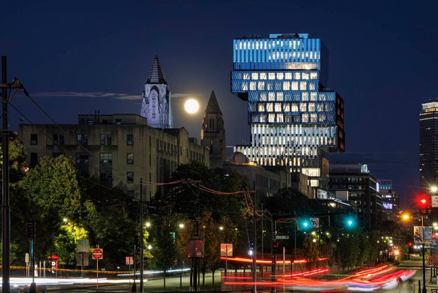Photo: View of the CDS building from Commonwealth Ave on October 9, 2022. Nighttime stock campus photo of Boston University campus shows street-view of cars and pedestrians on BU's campus. The city and CDS building can be seen brightly lit against the night scene.