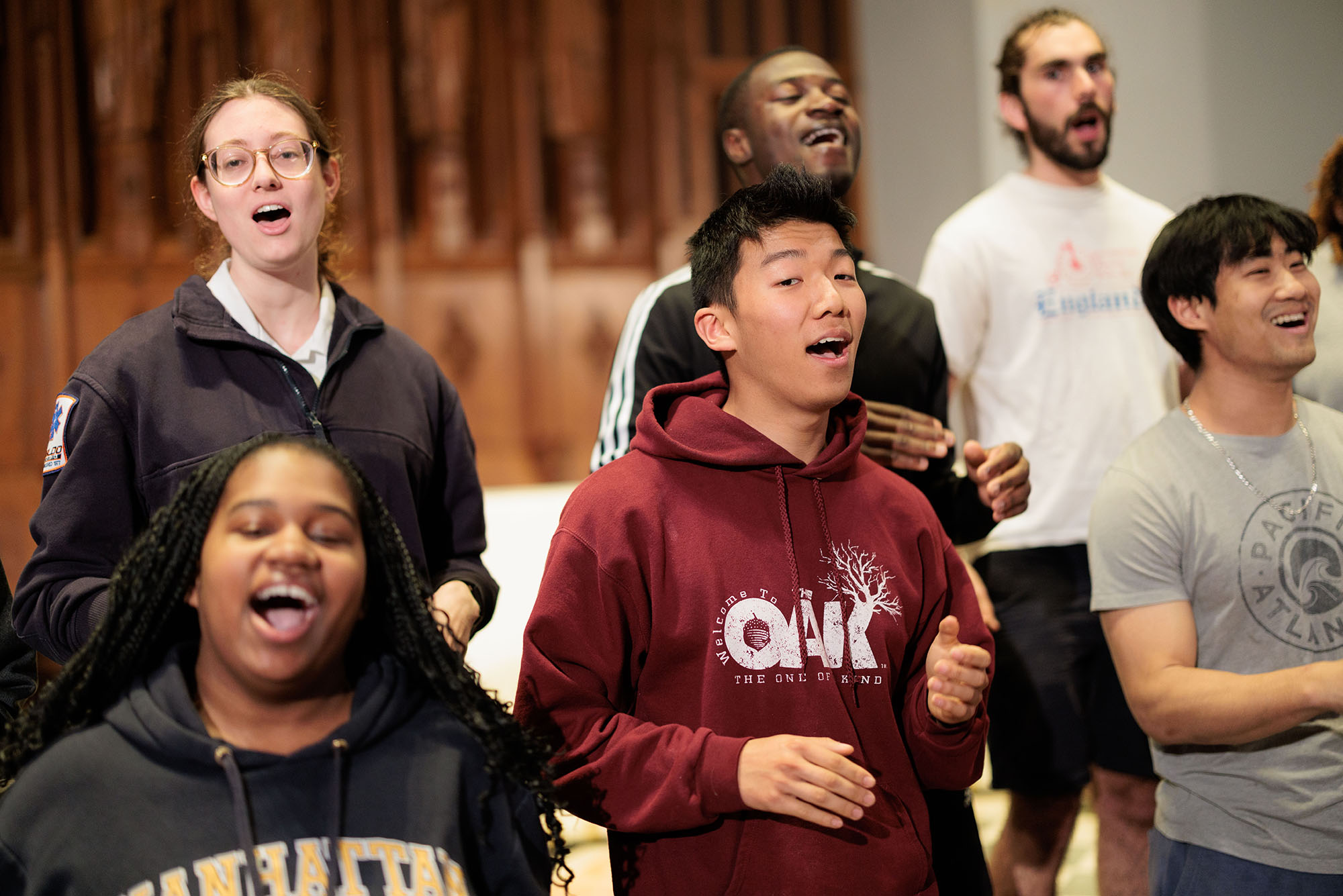Photo: Students with their mouth agape sing in BU's Inner Strength choir. The are practicing in a warm-up room and are wearing various comfortable clothes.