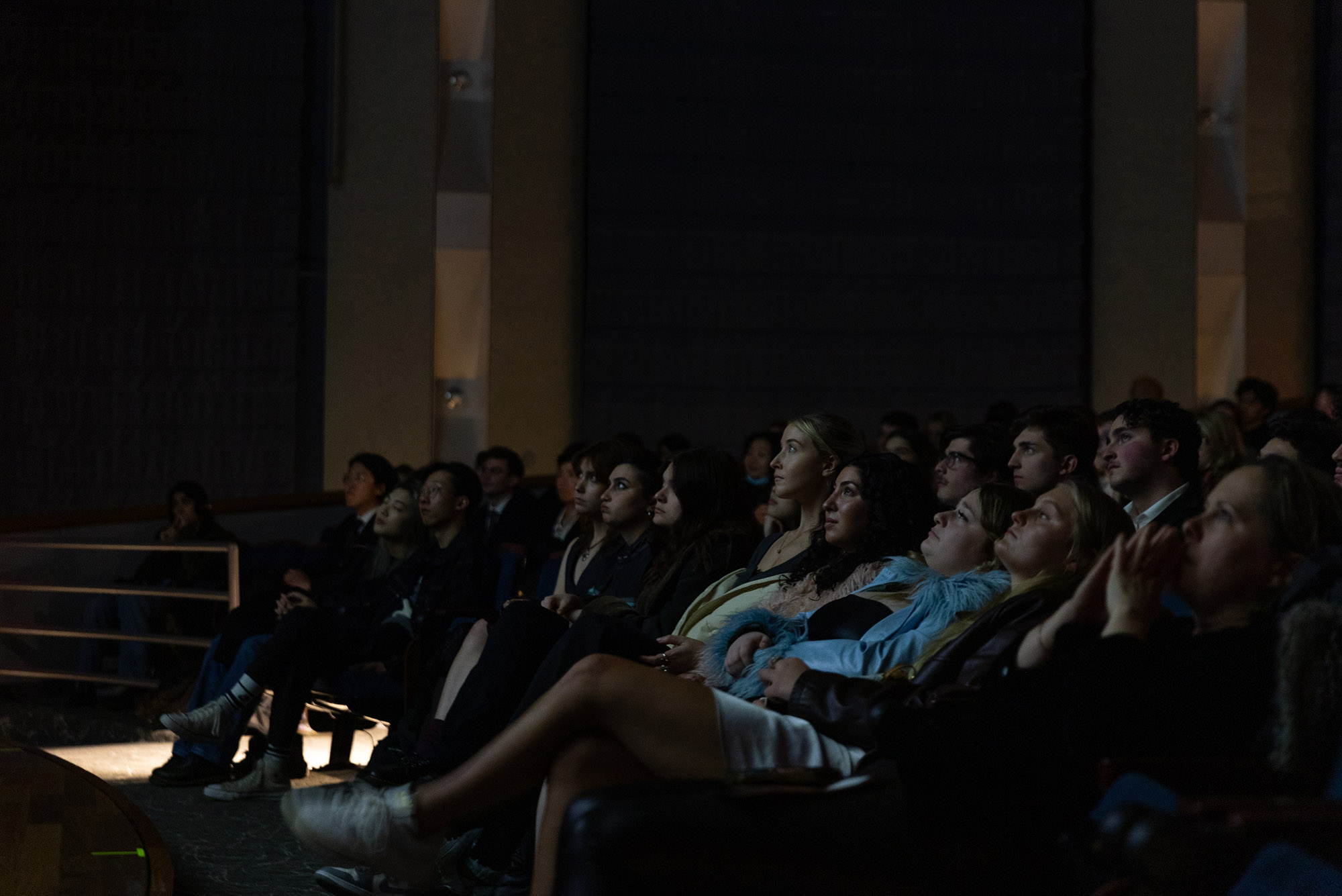 Photo: A dark theater with various people looking intently at the screen in front of them (not shown). They are all wearing different, comfortable outfits.