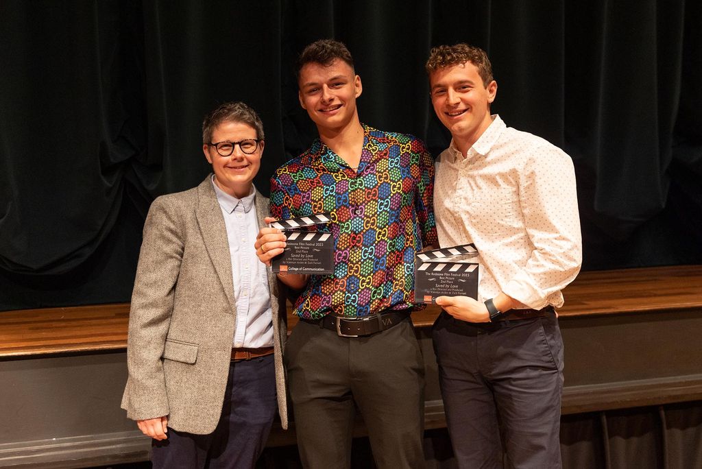 Photo: A group photo of the second-place award from the Redstone film festival. A white man on the left with a gray blazer and a blue button-up shirt. In the middle, a white man with a multi-colored button-up shirt, dark gray slacks smiles at the camera and holds a film cut award. And the man on the right wears a white button-up and dark gray slacks. He also smiles at the camera.