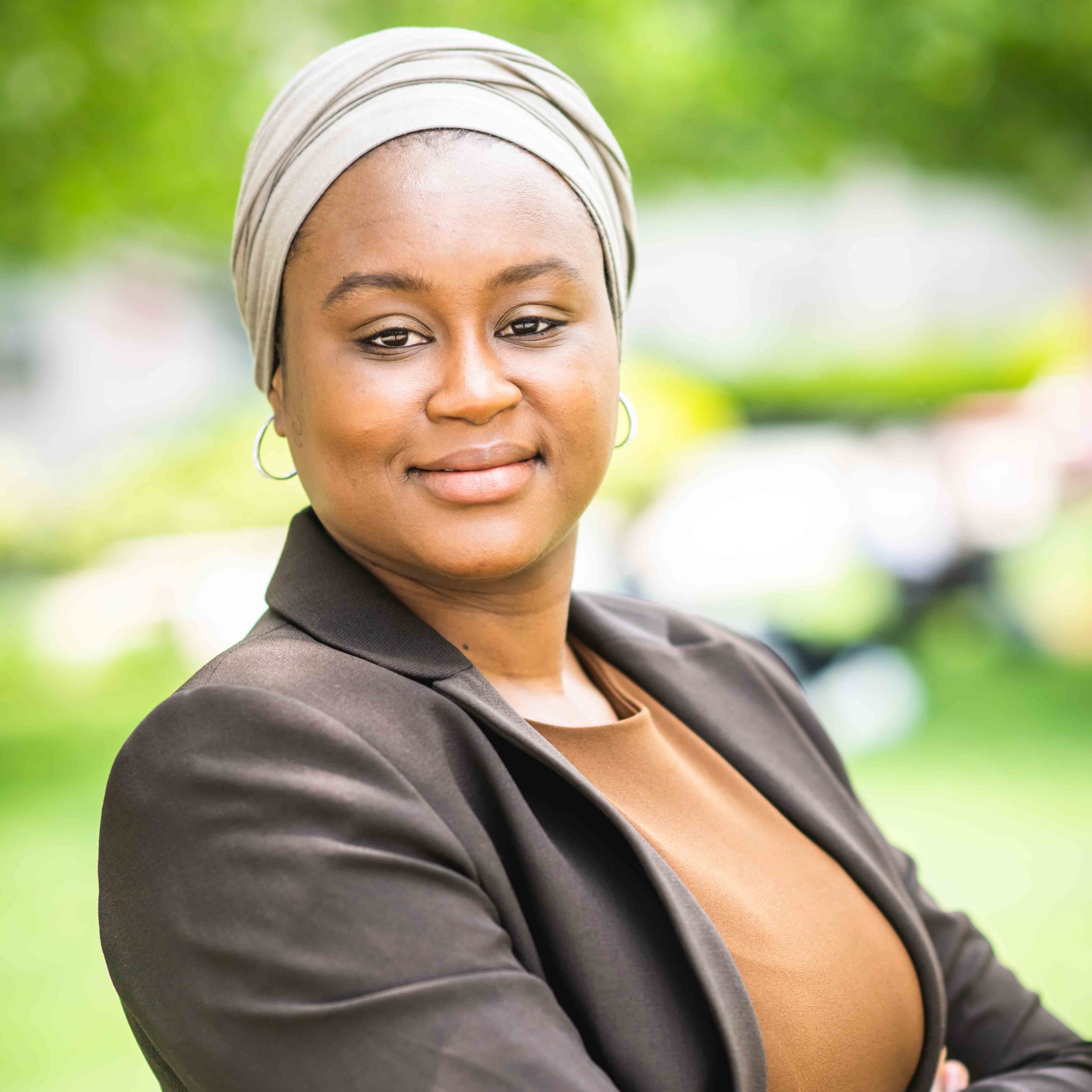 Photo: A black woman with her arms crossed wearing a headscarf and a brown blazer.