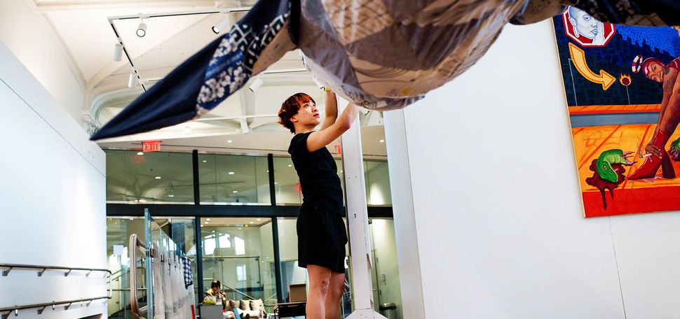 Photo: A young man wearing a black shirt and shorts works on a large sculpture being displayed in an art gallery.