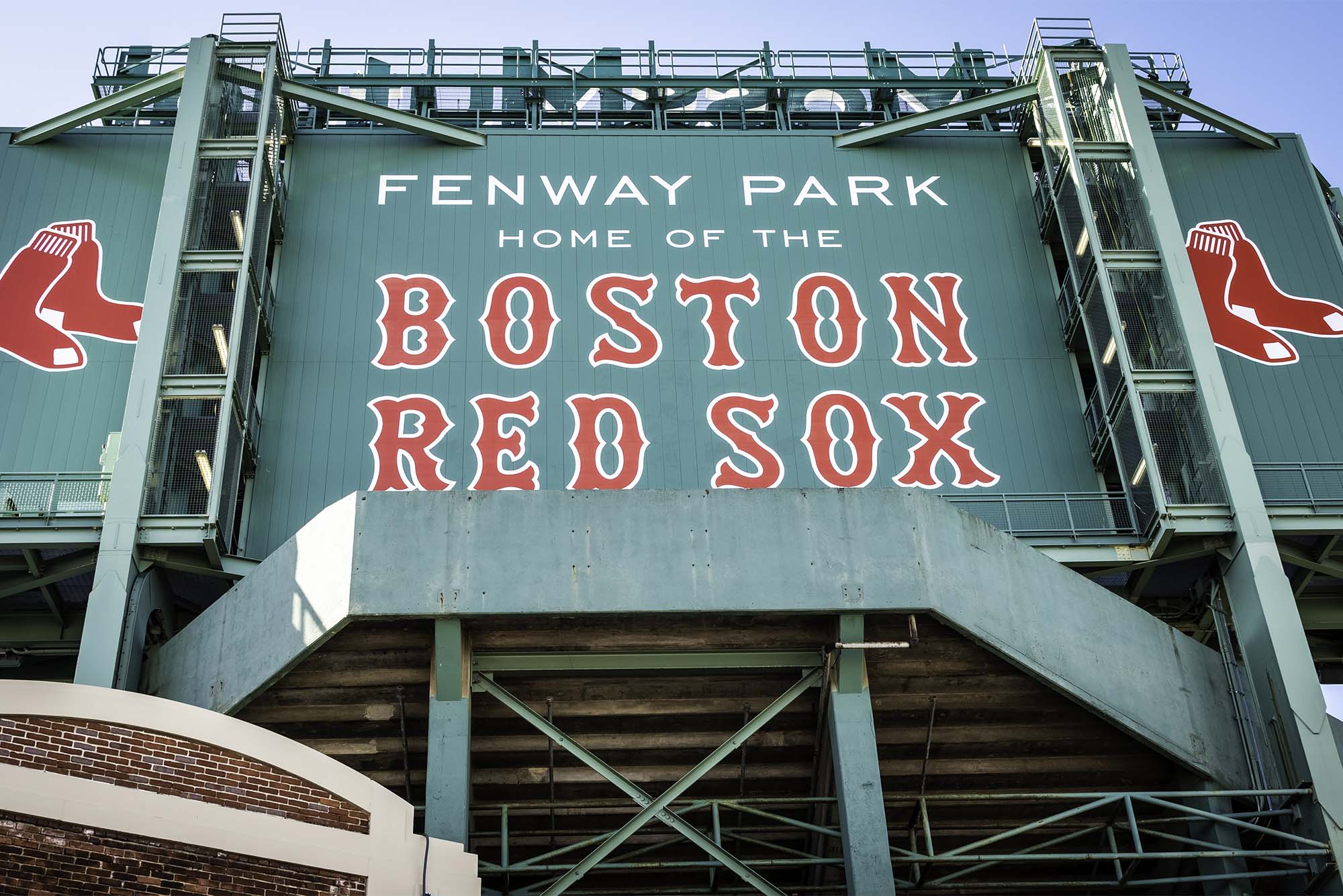 Photo: view of the historic architecture of the Fenway Park Stadium in Boston, Massachusetts, USA showcasing its sings and red brick walls on a sunny winter day. Text reads "Fenway Park, Home of the Boston Red Sox"