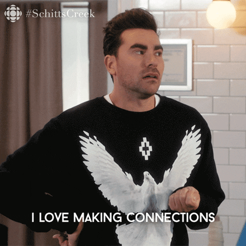 This is a GIF from a TV show called Schitts Creek. A male character from the show is putting his hands up and saying "I love making connections." There is a caption on the GIF that reiterates what he is mouthing. He is wearing a black sweater with a dove on it. (Pic creds: Giphy.com)