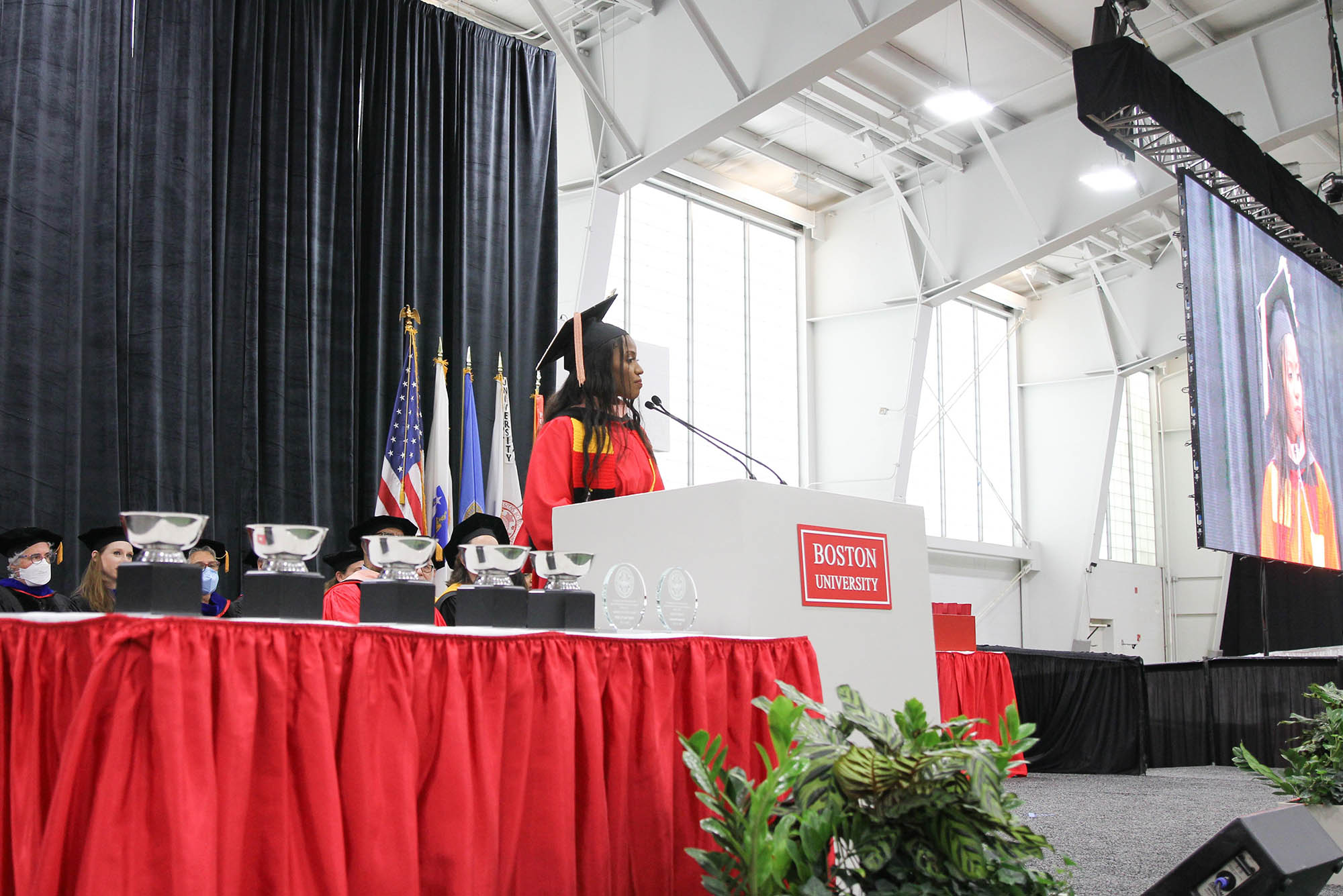 Photo: The student speaker, Daphne Nakawesi, a Black woman, addresses the crowd in her ceremonial cap and gown.