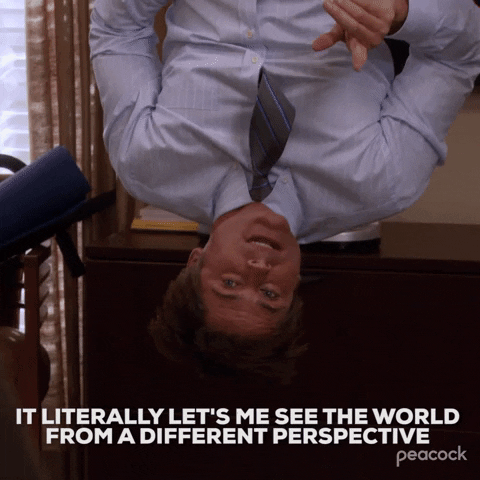 This is a GIF of a man hanging upside down with a dress shirt and tie on. He is speaking to people and moving his hands, saying "it literally let's me see the world from a different perspective." There is text that also reiterates what he is saying.