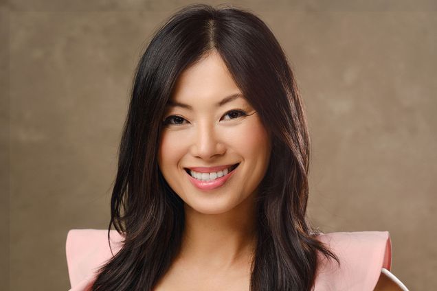 Photo: Jennifer Yen, an Asian woman with long black hair wearing a pink top, stands in front of a generic photo drop and smiles for the camera.