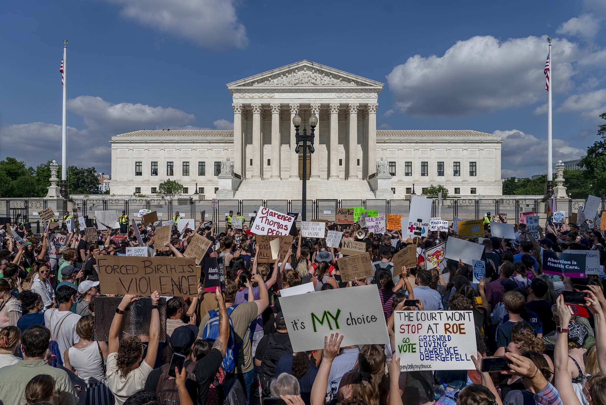 Photo: A crowd of protestors hold pro-choice signs as they protest and gather outside the fenced off Supreme Court.