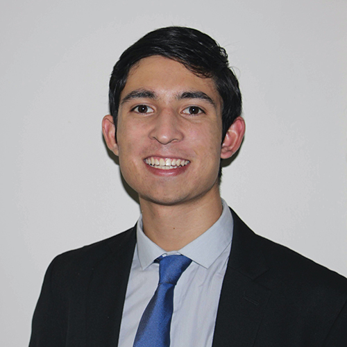 Photo: Headshot of Producer Alex Lo, a young man with black hair and wearing a black suit jacket, light blue collared shirt, and blue tie. He smiles and poses in front of a light grey background.