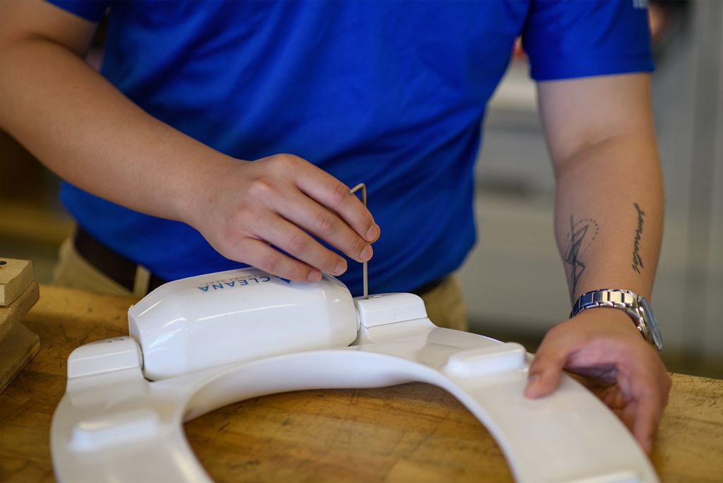 Photo: A person in a blue uniform screws in a a piece on a toilet seat lid