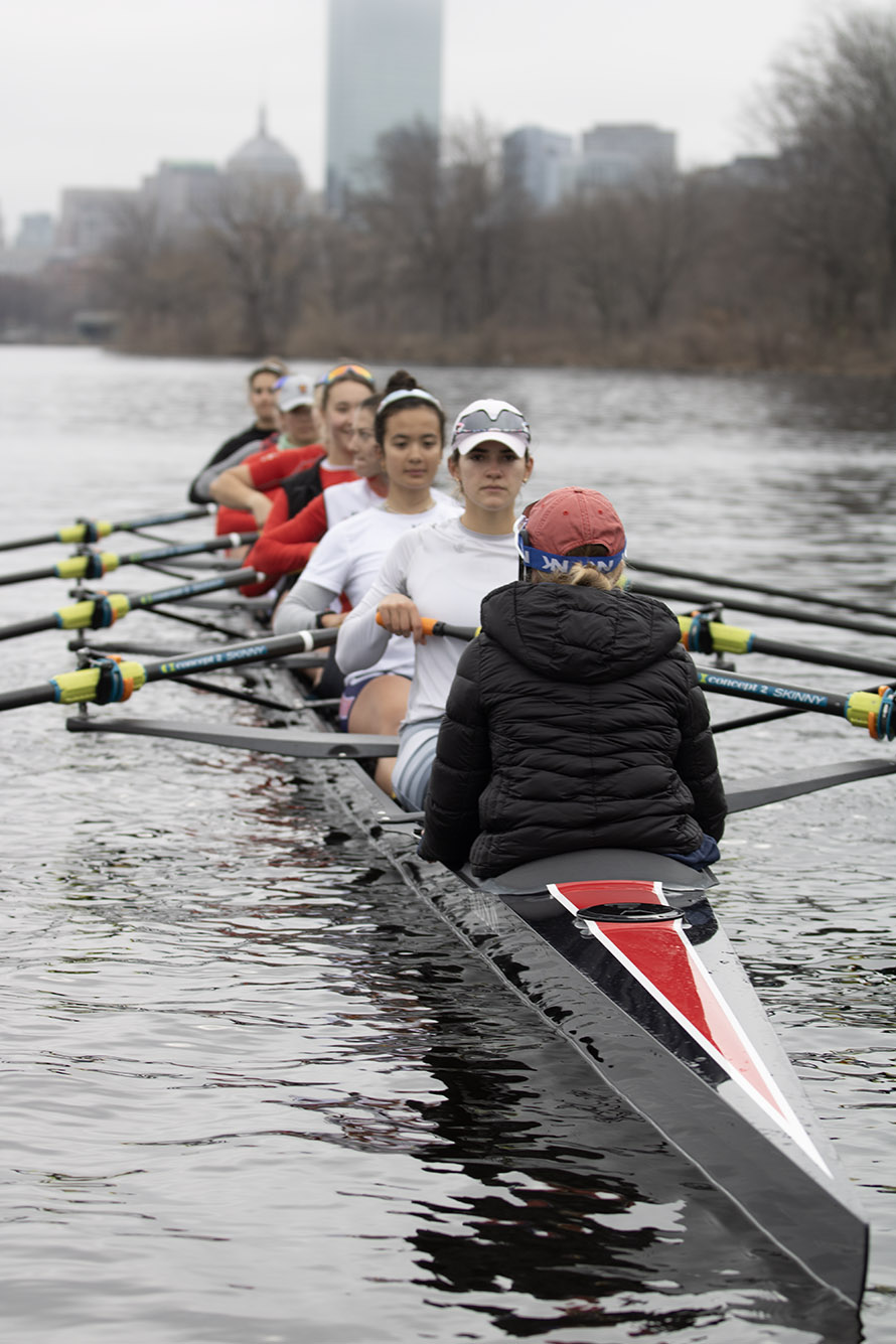 Photo: A boat full of women rowers are shown rowing down the Charles River in Boston on a gloomy day.