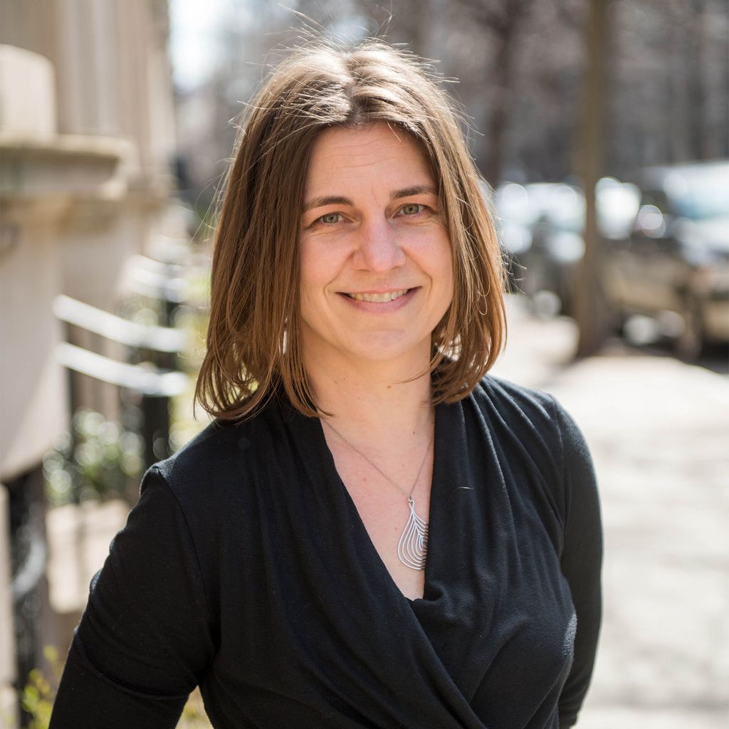 Photo of a woman with short dark hair standing outside on a sunny day in a black shirt