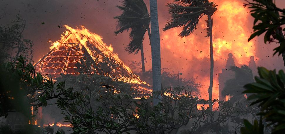 Photo: The hall of historic Waiola Church in Lahaina and nearby Lahaina Hongwanji Mission are engulfed in flames along Wainee Street. A large pyramid-shaped building and surrounding palm trees and land are shown engulfed in flames. Large flames are seen in the background as the sky looms red and black.
