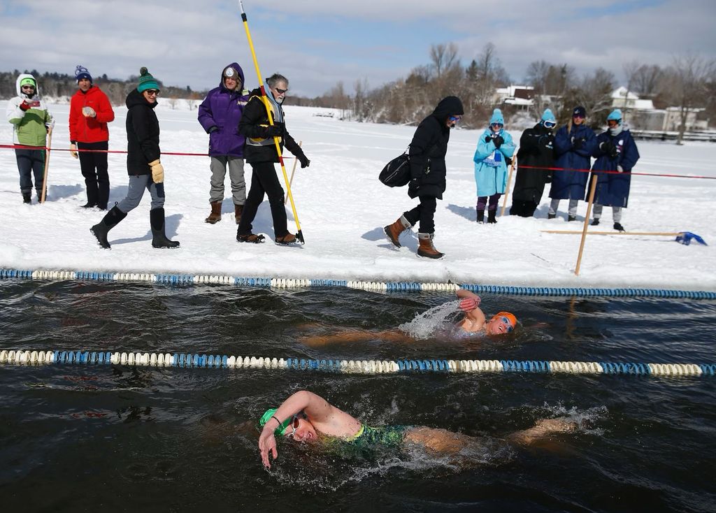 Photo: Laurie Craigen and another swim swim in opposite directions in lanes created at the edge of a snowy and icy terrain. Spectators and guides stand and watch at the icy edge.