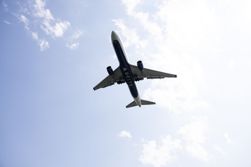 Photo: shot of a Delta plane flying overhead on a sunny, slightly cloudy day. The word "Delta" can be seen printed on the bottom of the plane.
