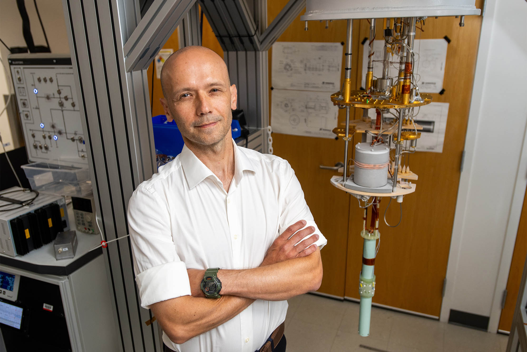 Photo: A bald man in a white collared short sleeve shirt stands with arms crossed