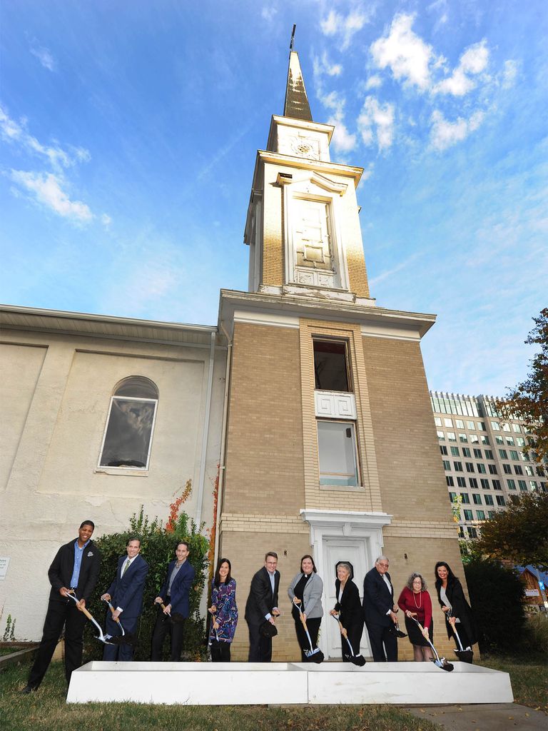 Photo: A group of people in suits holding shovels in front of a Church for a groundbreaking ceremony turning the church into apartments