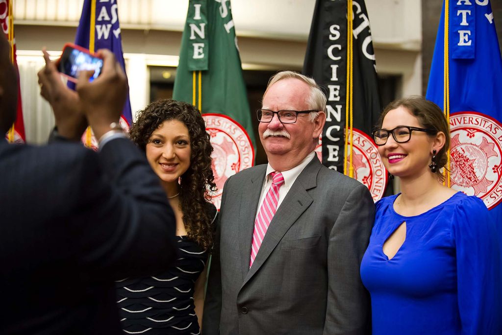 Photo of President Brown, center, taking a photo with two students during a breakfast he and Dean Elmore hosted for student group leaders. Brown wears a gray suit with a pink tie, has dark glasses and short gray hair. The young woman of color at his right has dark curly hair and wears a black dress. At his left, a White woman wears a blue dress, glasses, and has dark brown hair.