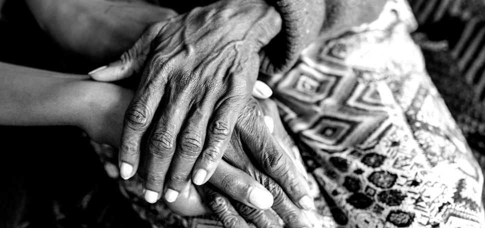 Photo: Black and white close up shot of an older, Black women's hands resting on a blanket.