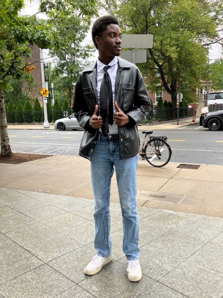 Photo: A tall student with dark, a black leather jacket, and a tie in blue jeans strikes a pose on a city street