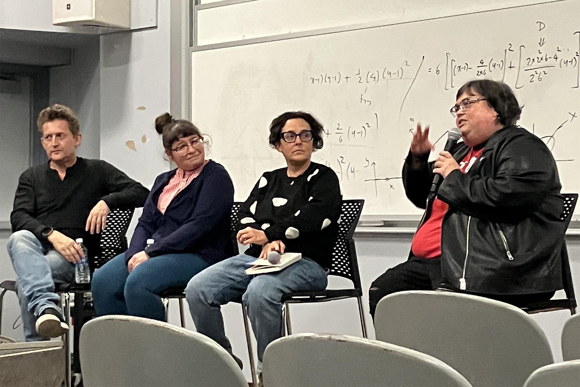 Photo: Four people on a stage answer questions in a panel format, with one holding the mic to speak to the auditorium