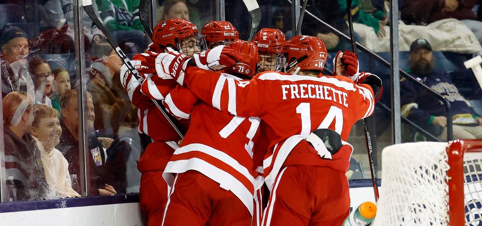 Photo: A group of four men dressed in red BU hockey gear hug and embrace on the ice rink at the end of a game.