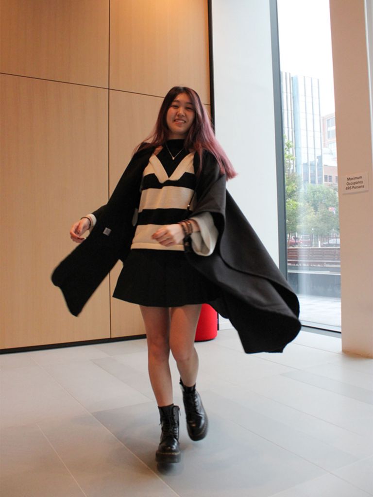 Photo: A student in a shirt, a striped shirt and a cape twirls for the camera