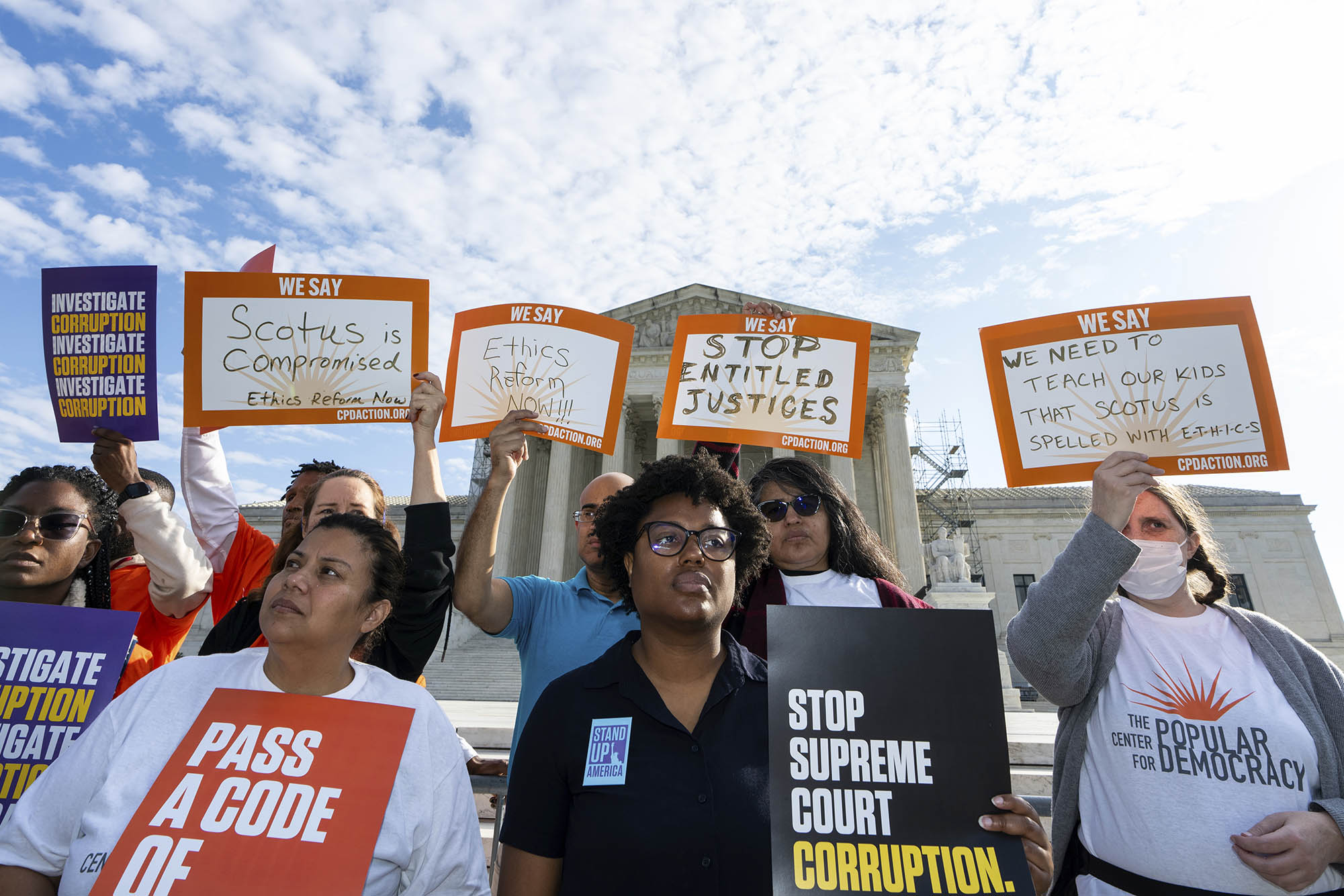 Photo: A diverse group of people holding signs protesting corruption in the Supreme Court and asking for a code of ethics are shown standing and protesting outside the Supreme Court building.